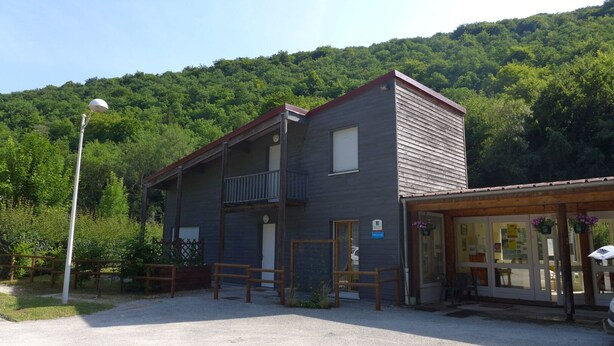 A two-story building with a balcony, a small porch, and a gravel driveway.