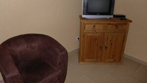 A room with a brown leather chair, a wooden cabinet with a television on top, and a tiled floor.