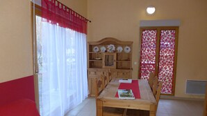 A cozy room with a wooden dining table, chairs, a red sofa, and a wooden cabinet with dishes.