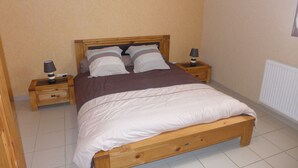 A single bed with a wooden frame, two bedside tables with lamps, a radiator, and a plain wall. - Vétus Villa - Viéville - Vacation Rental (Viéville)