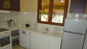 A compact kitchen with white appliances, including a microwave, dishwasher, stove, and refrigerator. There is a window above the sink, and the floor is tiled. - Vétus Villa - Viéville - Vacation Rental (Viéville)