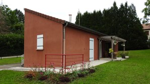 A small building with a red exterior, a white door, and a covered outdoor area with potted plants. - Vétus Villa - Viéville - Vacation Rental (Viéville)