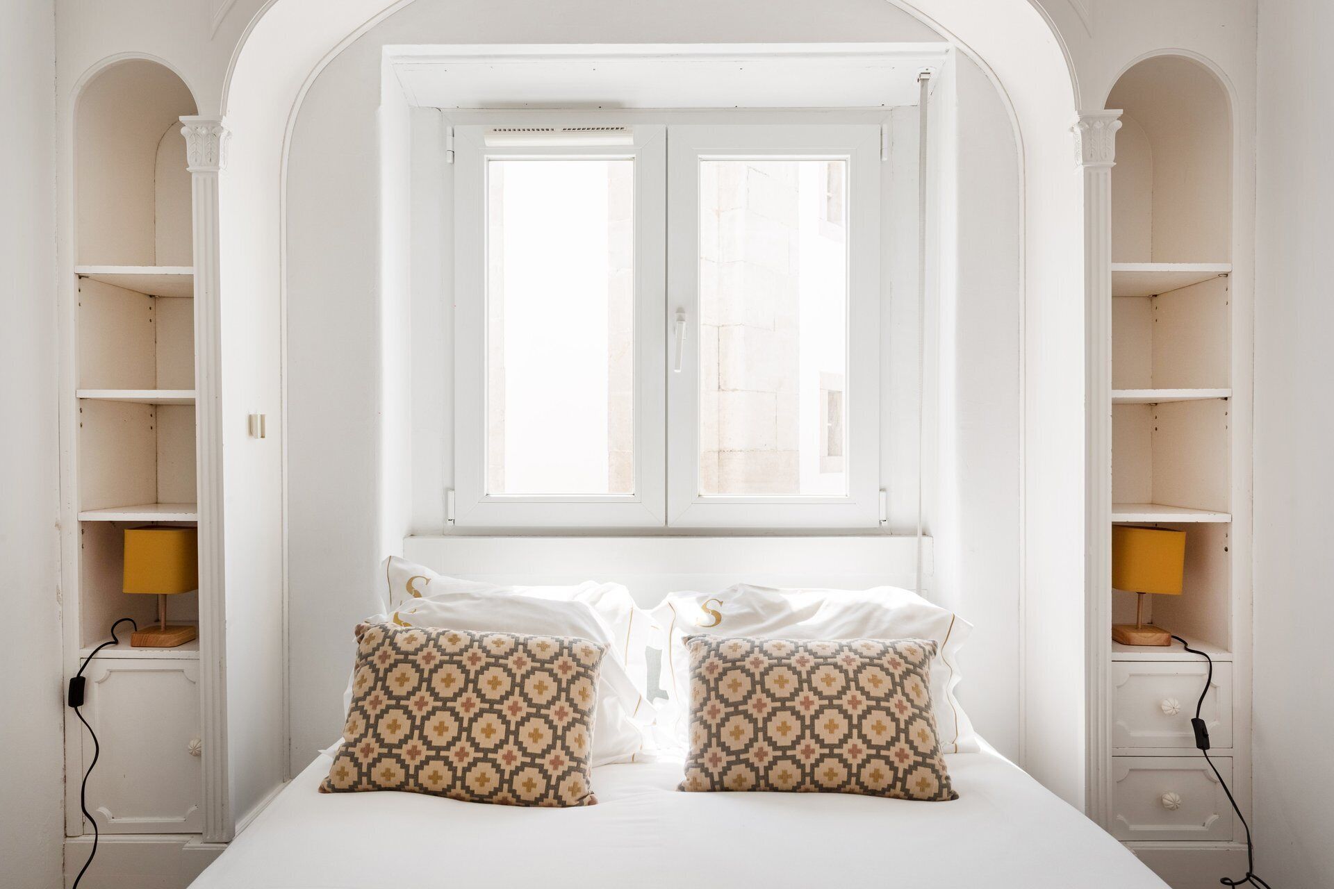 A bedroom with a bed, two patterned pillows, a window, and built-in shelving.