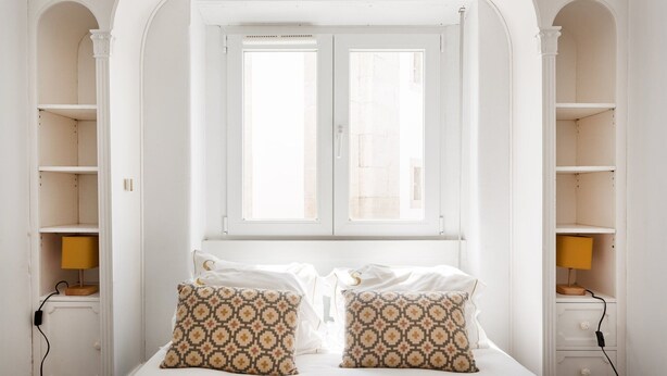 A bedroom with a bed, two patterned pillows, a window, and built-in shelving. - Yellow Suites Duplex @ Cascais Historical Center (Cascais)