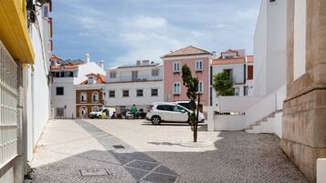 A cobblestone street with buildings, a parked car, and a person walking.