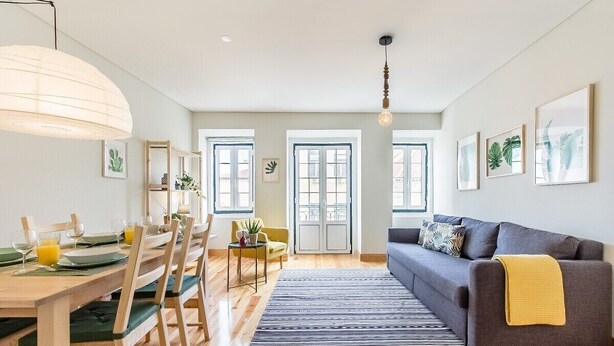 Una sala de estar moderna con comedor, piso de madera, un sofá gris y un ventanal grande.
