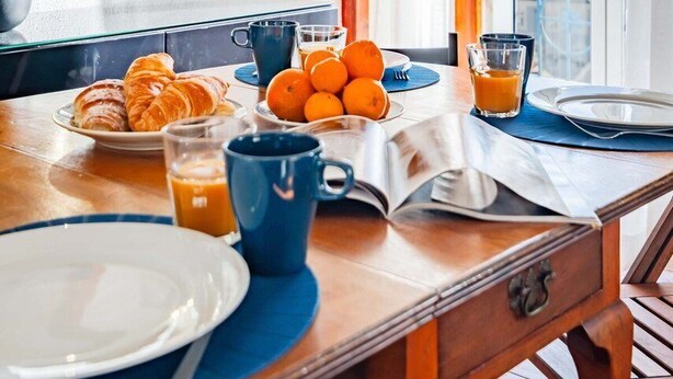 Ein Frühstückstisch mit Croissants, Orangen, Saftgläsern, einem Buch und einem Glas Orangensaft.