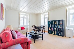 Ein Wohnzimmer mit einer Couch, einem Couchtisch, einem Esstisch mit Stühlen, einem Bücherregal und einem Fenster.