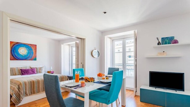 A modern living room with a dining area, a bed, a TV, and a large window. - Lisbon Prime Apartment (Lisbon)
