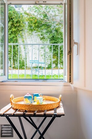 Ein Fenster mit Blick auf Grünflächen, ein Tisch mit einem Korb und ein Stuhl draußen.