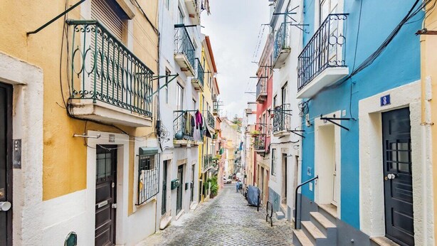 Una estrecha calle adoquinada bordeada por edificios coloridos con balcones y puertas.