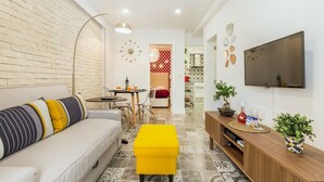 Una sala de estar moderna con sofá, reposapiés, televisor y un comedor con sillas y mesa.