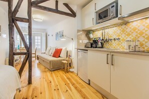Eine kleine Küche mit Mikrowelle, Toaster und Spüle. Holzbalken sind sichtbar, und der Raum ist in einer neutralen Farbgebung gehalten.