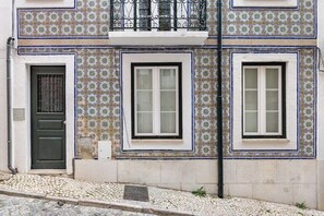 A building with patterned tile walls, a balcony with a wrought iron railing, and a cobblestone street. - Studio Mar, in the Heart of Lisbon (Lisbon)