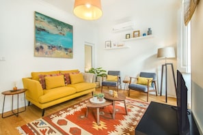 Ein Wohnzimmer mit gelber Couch, Couchtisch, Fernseher und einem Gemälde an der Wand.