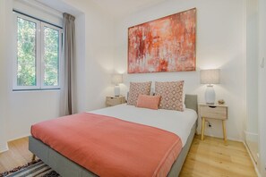 Ein Schlafzimmer mit einem Bett, zwei Nachttischen, einem Fenster und einem abstrakten Gemälde.