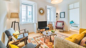 Una sala de estar con televisor, sofá, sillón y una alfombra estampada.