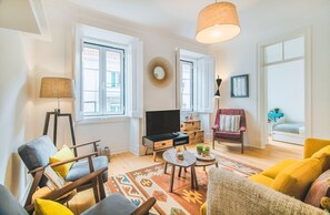 Ein Wohnzimmer mit Fernseher, Sofa, Sessel und einem gemusterten Teppich.