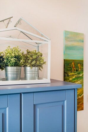 Ein blauer Schrank mit einem Blumentisch in weißem Rahmen und einem Bild an der Wand.