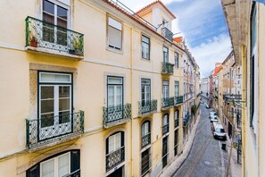 Uma rua estreita ladeada por edifícios, com varandas e grades de metal, e um pavimento de calçada.