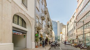 Eine schmale Stadtstraße mit mehrstöckigen Gebäuden, einem sichtbaren Hauseingang mit einem grünen Schild und abgestellten Rollern.