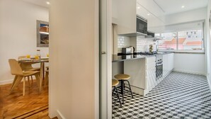 Eine moderne Küche mit einem schwarz-weißen Schachbrettboden, einem Essbereich mit Tisch und Stühlen sowie einem Ausblick durch ein Fenster.