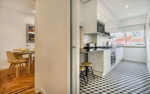 Eine moderne Küche mit einem schwarz-weißen Schachbrettboden, einem Essbereich mit Tisch und Stühlen sowie einem Ausblick durch ein Fenster.