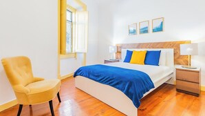 Ein Schlafzimmer mit einem Bett, einem Sessel, einem Nachttisch, einer Lampe und einem Fenster.