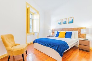 Ein Schlafzimmer mit einem Bett, einem Sessel, einem Nachttisch, einer Lampe und einem Fenster.