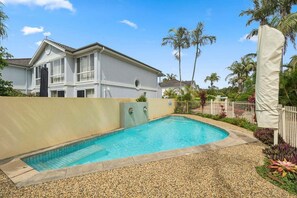 A swimming pool with a pebble border, a white building with a balcony, and palm trees in the background. - The Lazy Tide-Opposite Park Beach, Sleeps 6. Walk to clubs (Coffs Harbour)