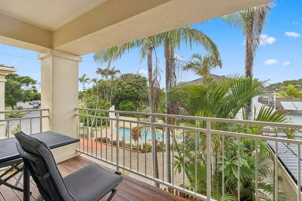 A balcony with a view of a swimming pool, palm trees, and a distant building. - The Lazy Tide-Opposite Park Beach, Sleeps 6. Walk to clubs (Coffs Harbour)