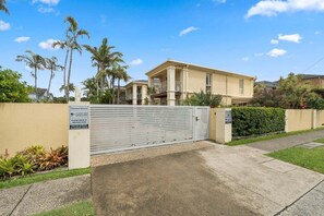 A gated residential property with a beige house, palm trees, and a clear sky. - The Lazy Tide-Opposite Park Beach, Sleeps 6. Walk to clubs (Coffs Harbour)