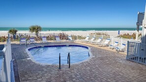 Ein Schwimmbecken mit Blick auf den Strand, umgeben von Liegestühlen und einem Zaun.