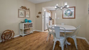 A dining area with a round table and white chairs, a white cabinet with decorative items, and a wooden floor. - Intracoastal Townhome with Private Entrance, Beach Equipment, and Bikes! (Indian Shores)