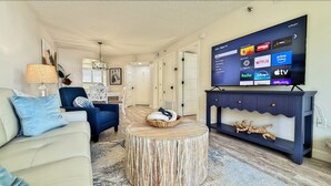 A living room with a flat-screen TV displaying streaming services, a sofa, a chair, a coffee table, and a decorative console. - Quintessential Beachfront Condo escape right on the Sand with private balcony (New Smyrna Beach)