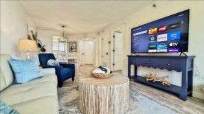 Un salon équipé d’un téléviseur à écran plat diffusant des services de streaming, d’un canapé, d’un fauteuil, d’une table basse et d’une console décorative.