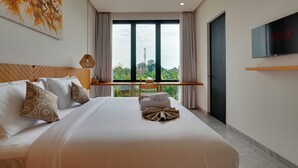 A hotel room with a large bed, a TV mounted on the wall, and a view of greenery outside. - Villa Vibhava - Umalas (Seminyak)