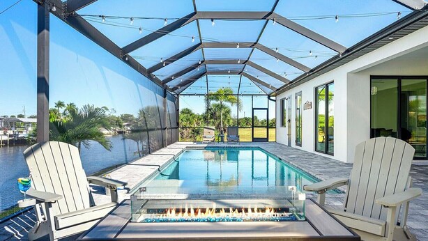 Una piscina scoperta coperta con un recinto in vetro, due poltrone Adirondack e un elemento decorativo a fuoco.
