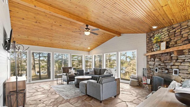 A spacious living area with a stone floor, a large gray sectional sofa, a stone fireplace, and a stone wall shelf. - Little House on Hickory (Lowell)