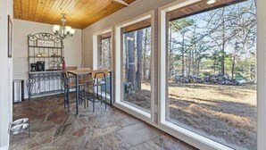 A cozy interior with a stone floor, wooden ceiling, and large windows offering a view of the outdoors. - Little House on Hickory (Lowell)