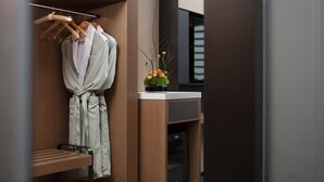 Un baño moderno con tocador de madera, una bata colgada en un perchero y una pequeña planta en maceta sobre el mostrador.