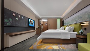 Habitación de hotel con una cama grande, un escritorio con televisor de pantalla plana, una zona de estar con un sillón y una pared con un mural de la ciudad.