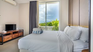A modern hotel room with a large bed, a TV on a wooden console, and a balcony with a view of greenery. - Bhiseka Villa Nusa Dua by Aishwarya Bali (Nusa Dua)