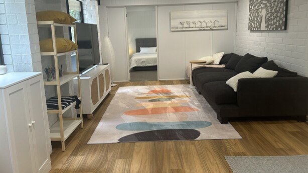 Un espacio habitable compacto con un sofá, un televisor, una estantería y una cama.