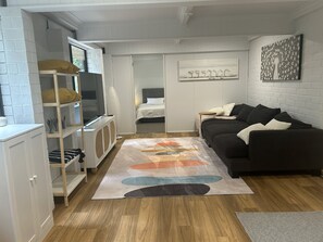 Un espacio habitable compacto con un sofá, un televisor, una estantería y una cama.