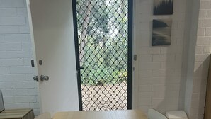 Una sala de conferencias con una gran mesa de madera, sillas blancas, una pared de ladrillo blanco y una puerta con mosquitera de metal.