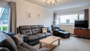 A modern living room with a leather sofa, a recliner, a coffee table, and a TV. - Glan Heulog - 3 Bed Holiday Home - Saundersfoot (Saundersfoot)