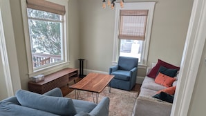 Ein Wohnzimmer mit einem blauen Sofa, einem Holztisch, einem blauen Sessel und einem grauen Sofa mit bunten Kissen.
