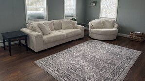 Ein Wohnzimmer mit zwei hellbeigen Sofas, einem dunklen Holztisch und einem gemusterten Teppich.