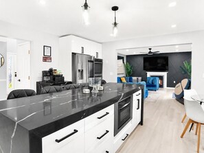A modern kitchen with a marble island, built-in appliances, and a dining area with a white table and chairs. - LUXE HAUS· Sleeps 12· Private Spa · 2 Game Rooms w Arcade & Theater · Playground (Tobyhanna)